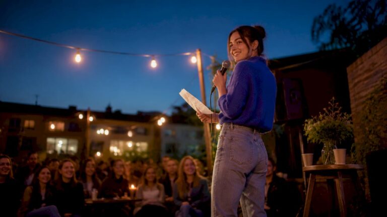 En ung kvinna står på scenen och kör standup, med sitt manus i handen.