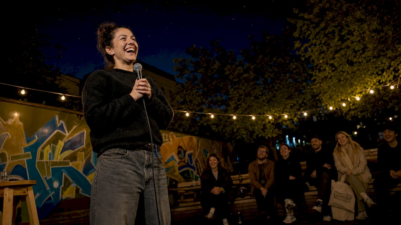 1781223306180_Standup-komiker-pa-scen-levererar-skamt En komiker står på scen och drar skämt inför publiken.